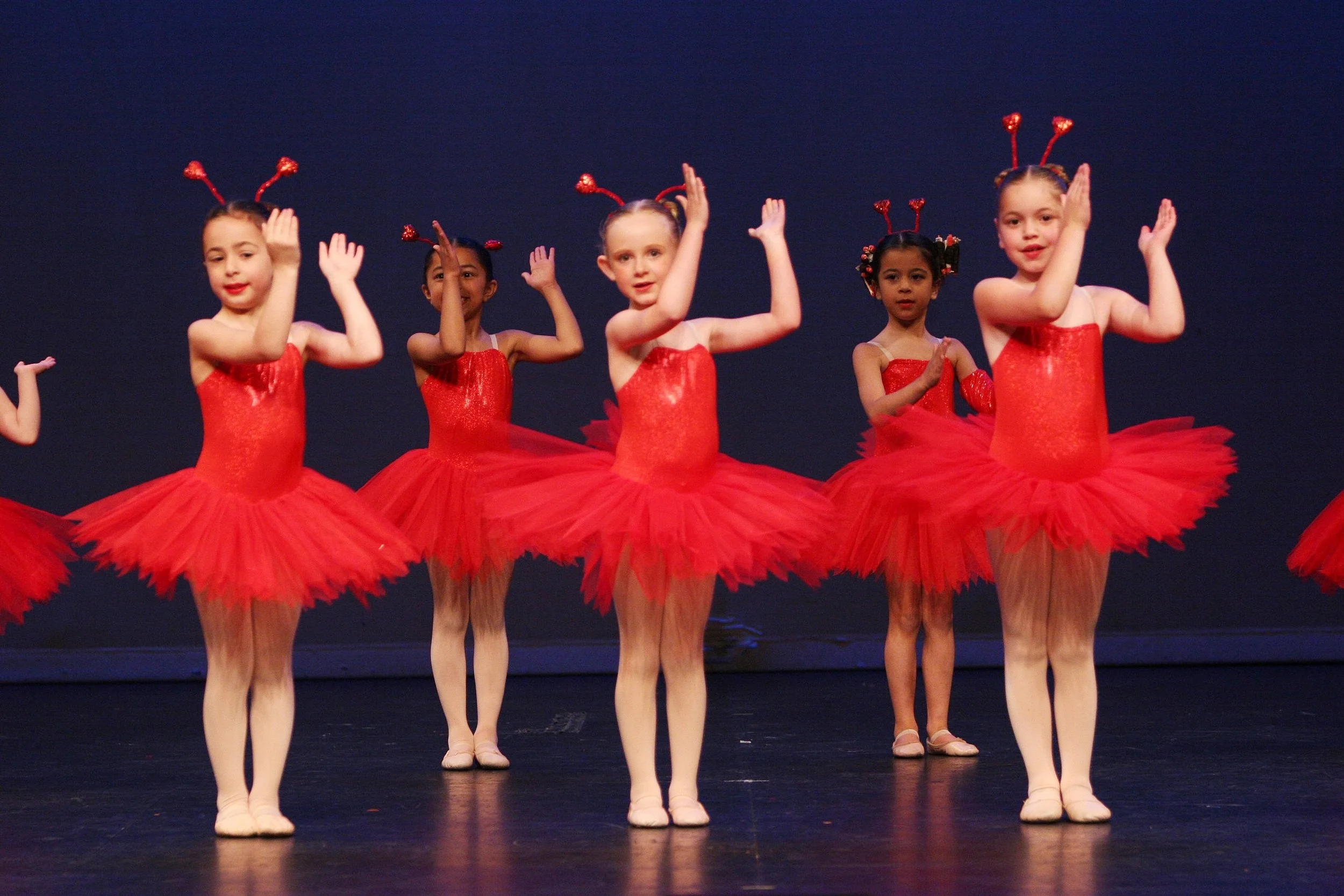 Young girls in red tutus and antler headbands performing a ballet on stage.