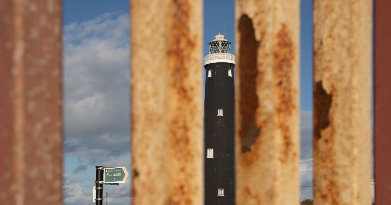 Old Lighthouse at Dungeness viewed through heavy iron gates 