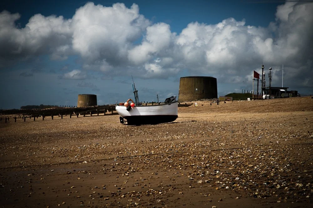 Fisherman's Beach at Hythe, Kent showing a clinker built wooden commercial fishing boat with two Martello Towers in the background