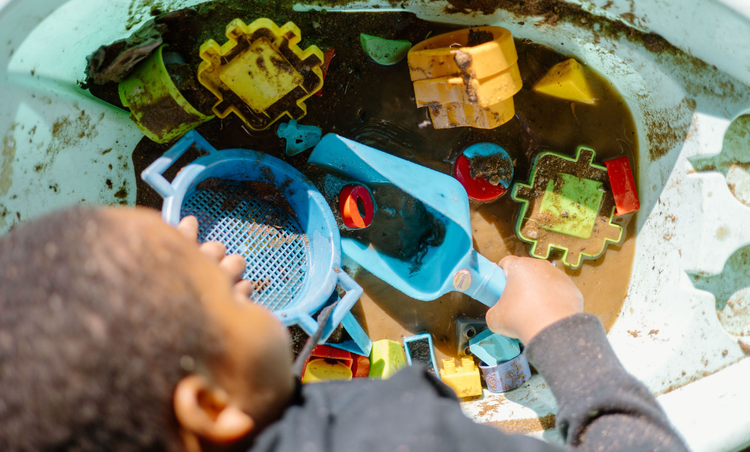 Child playing with dirty plastic toys and sand in a sandbox.
