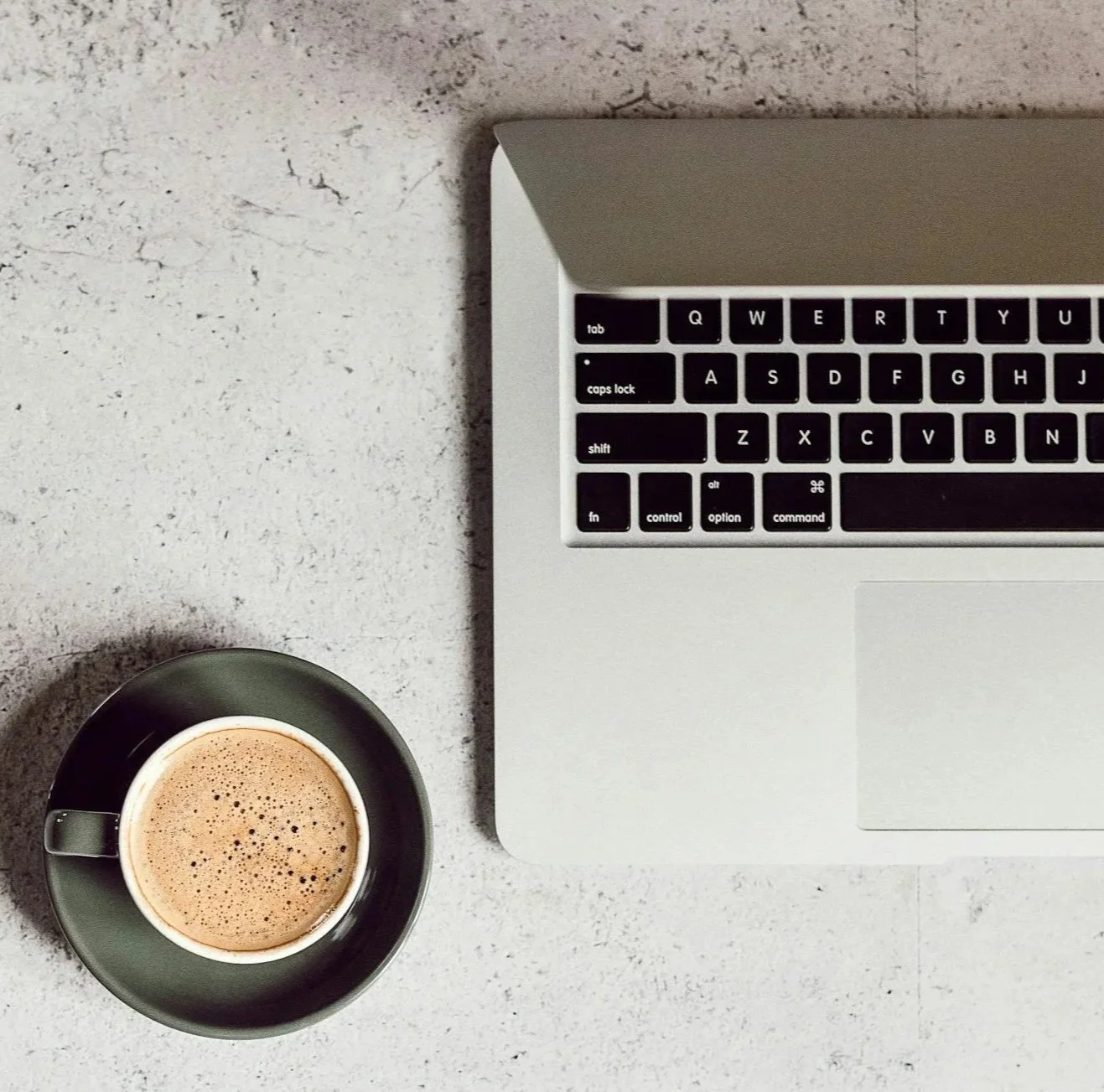 A laptop keyboard and a cup of coffee on a light-colored textured surface.