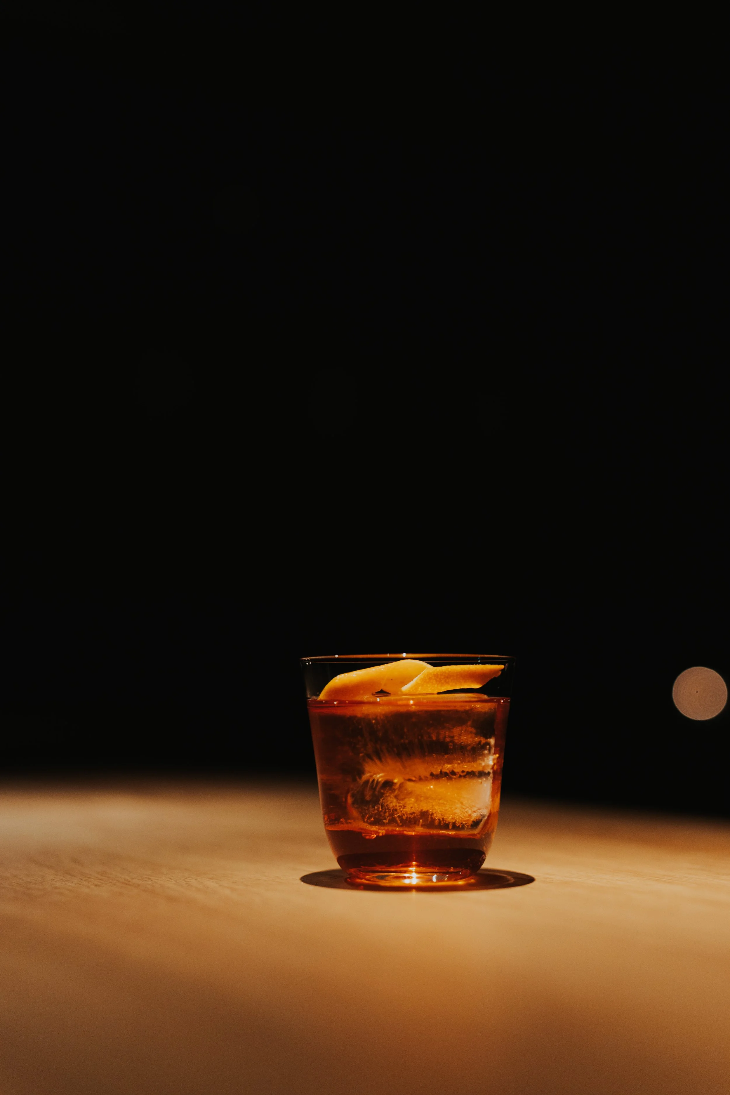 Ein Glas mit rotem Getränk und Eiswürfeln auf einem Holztisch bei Dunkelheit.