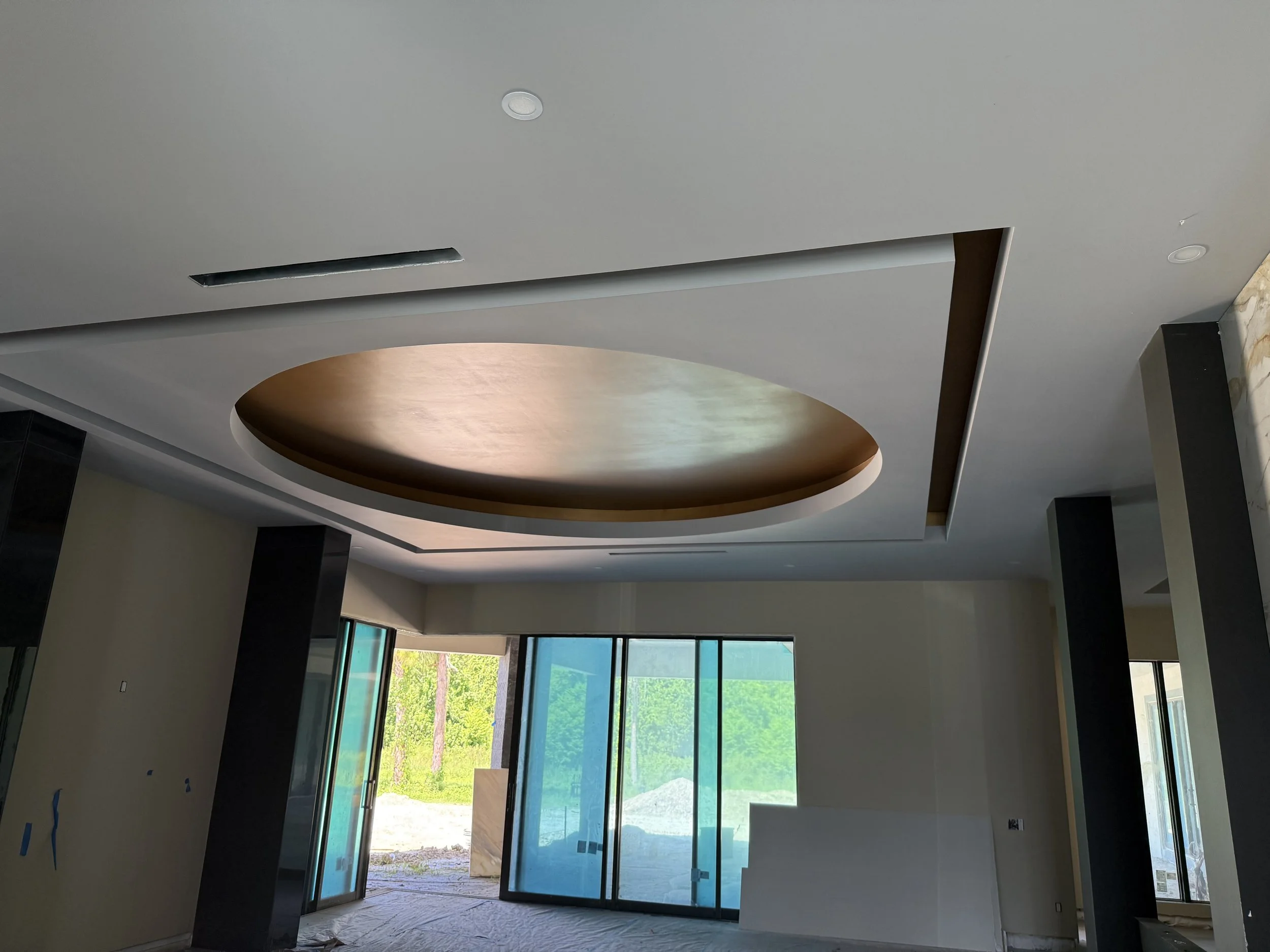 Interior of a modern room with large glass doors, a round recessed ceiling feature, and black columns.