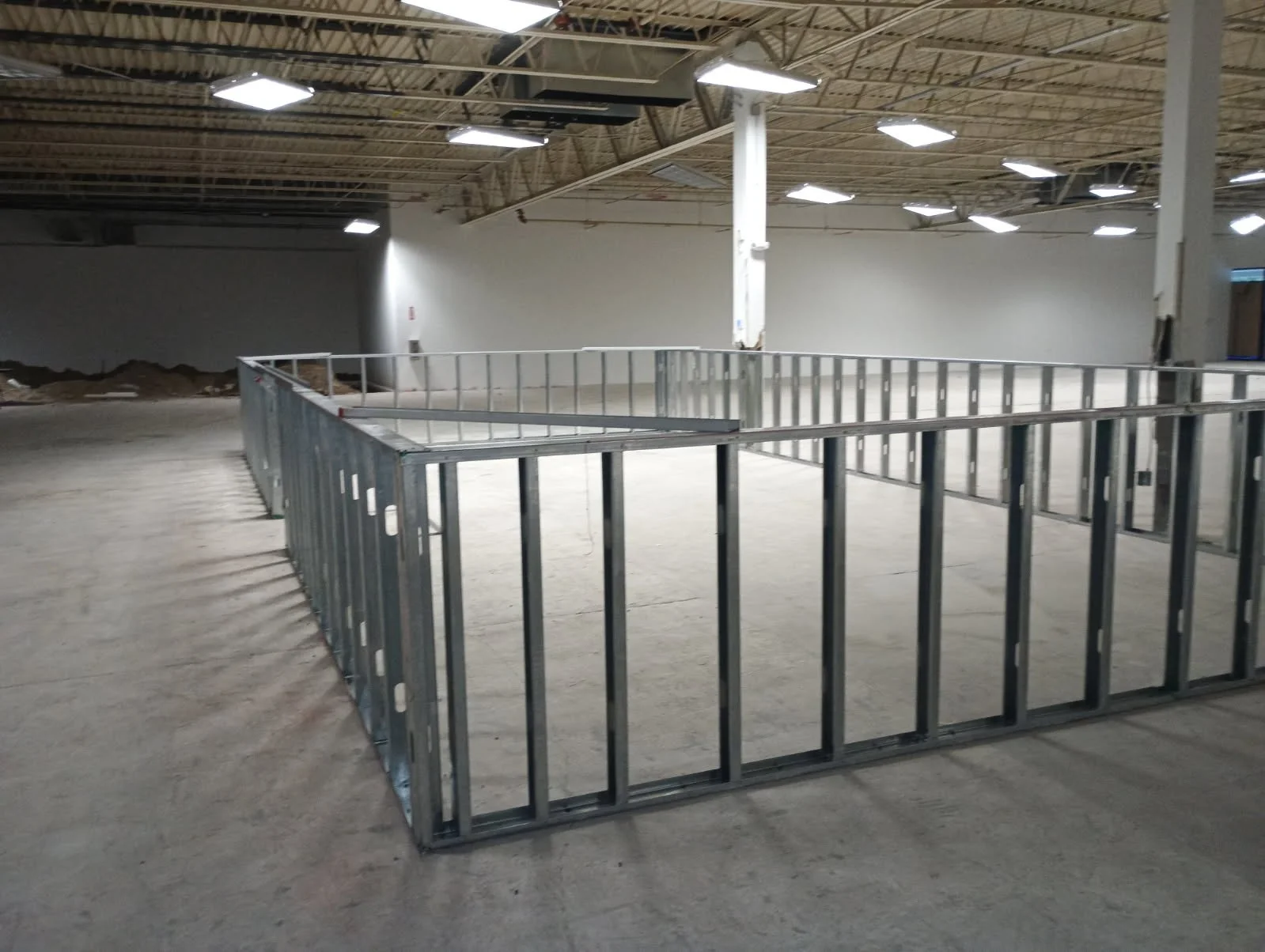 Interior of a large commercial or industrial building under construction with metal framing on the floor and exposed ceiling with lighting fixtures.