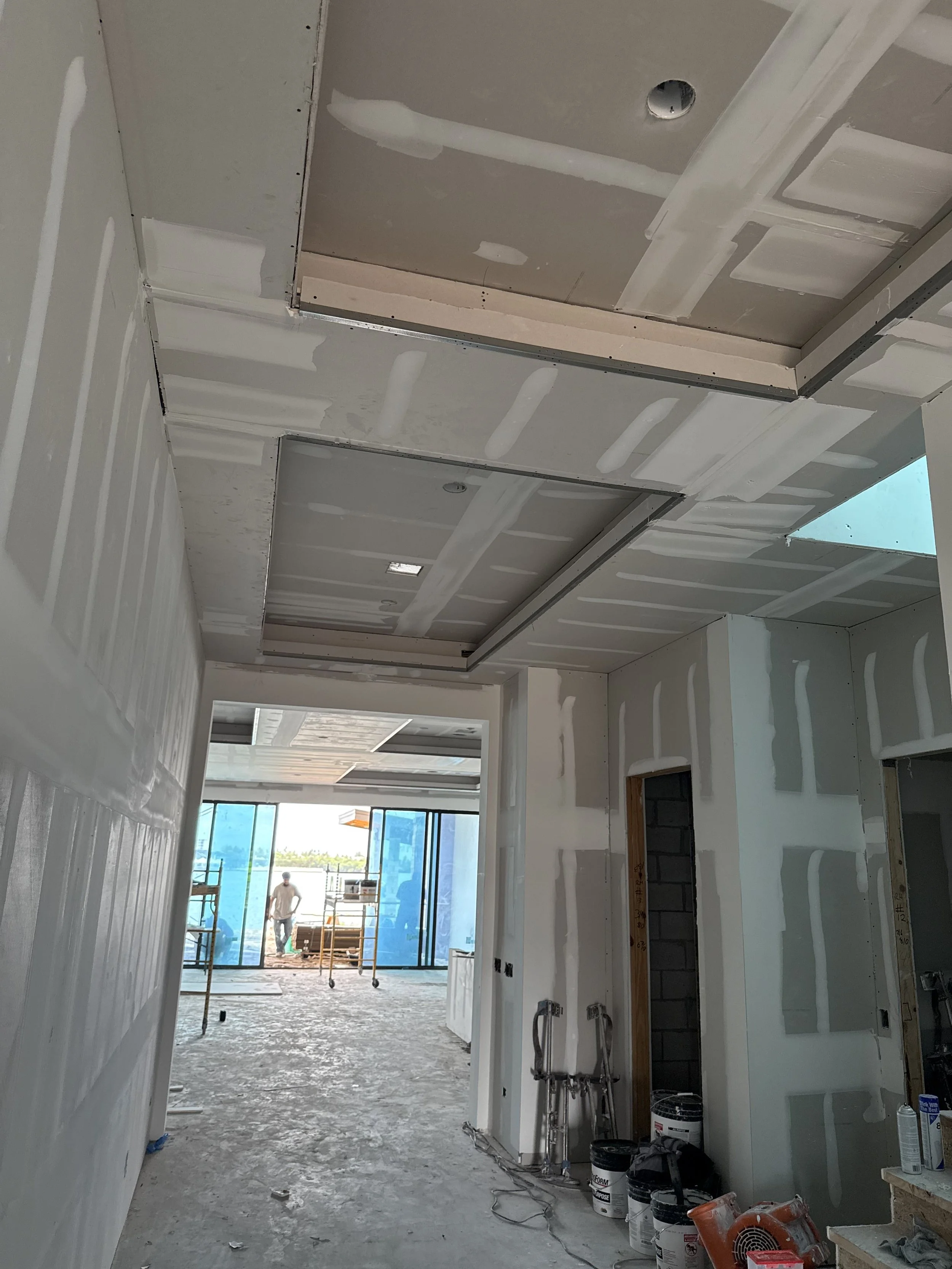 Interior of a building under construction with drywall installed, some tools and construction materials on the floor, and scaffolding near the windows.