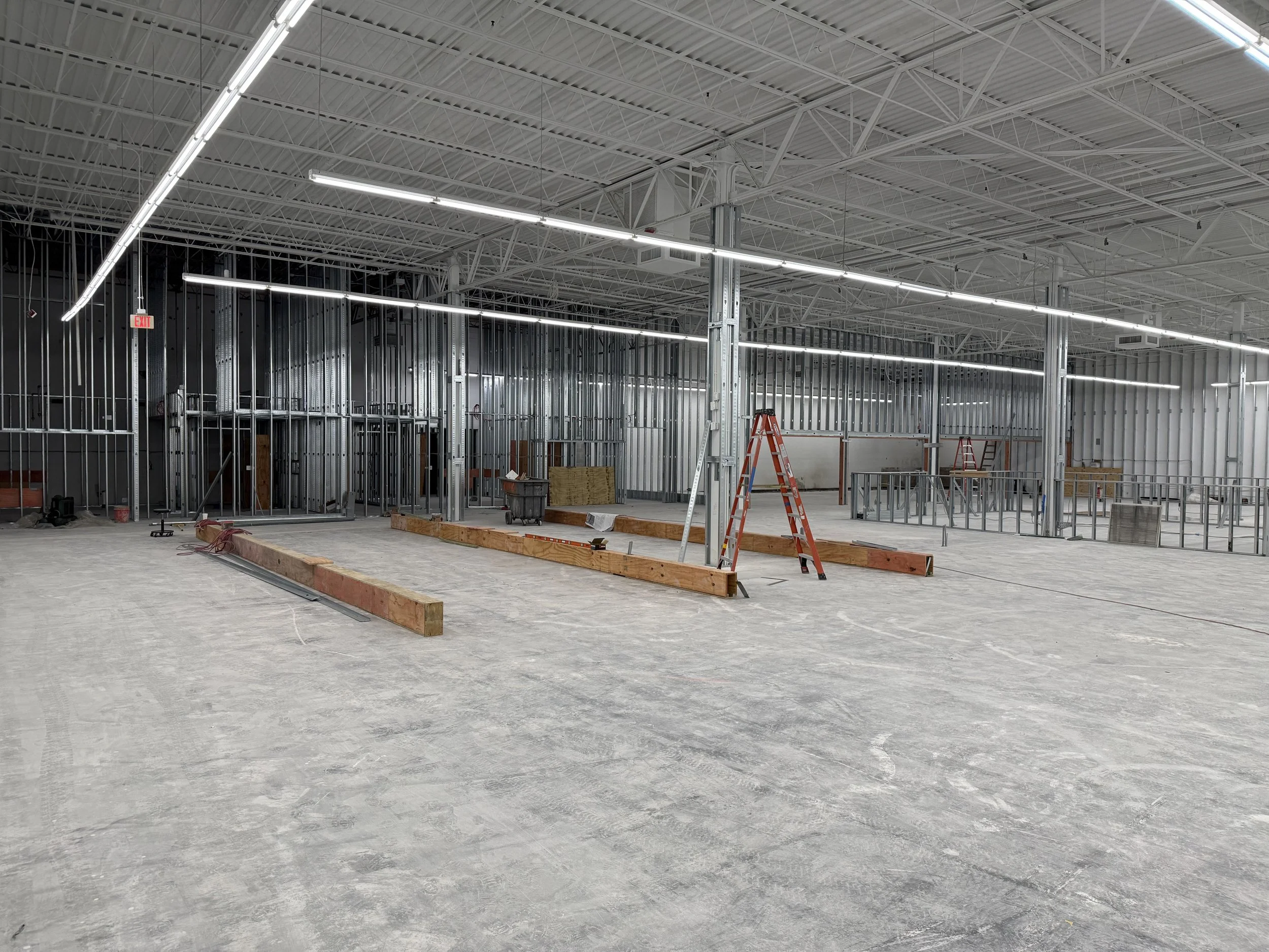 Interior view of a construction site with metal framing, ladders, wooden beams, and tools, indicating ongoing building work.