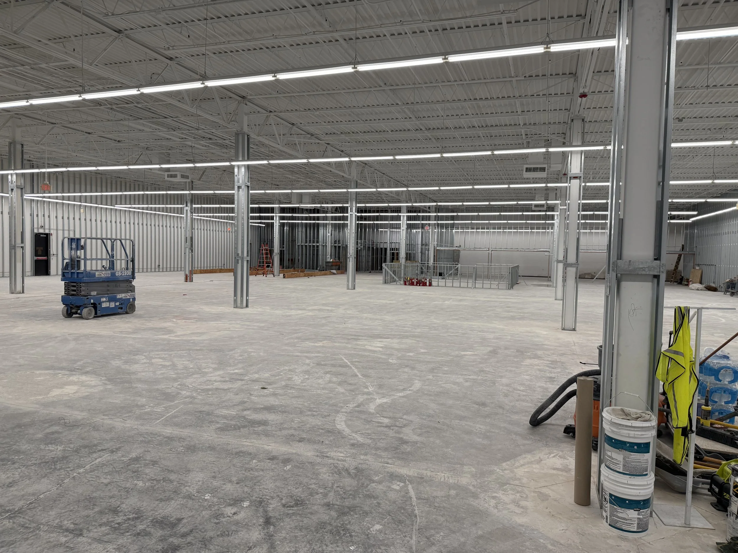 Interior of a large commercial or industrial building under construction with exposed metal framing, unfinished concrete floor, construction tools, and equipment.