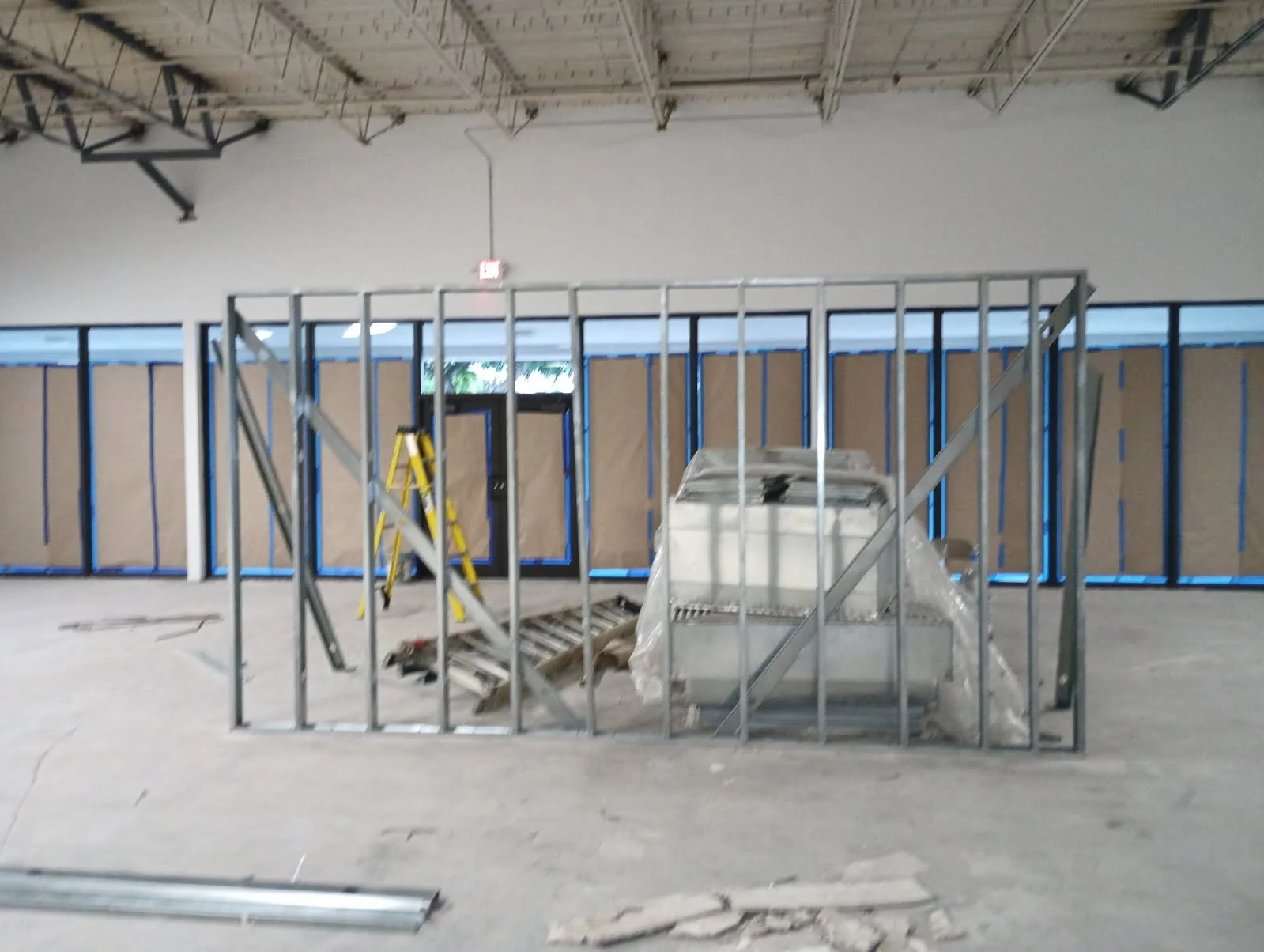 Construction site with metal framing, a yellow ladder, and partially enclosed wall with brown sheathing, inside a building under renovation or setup.