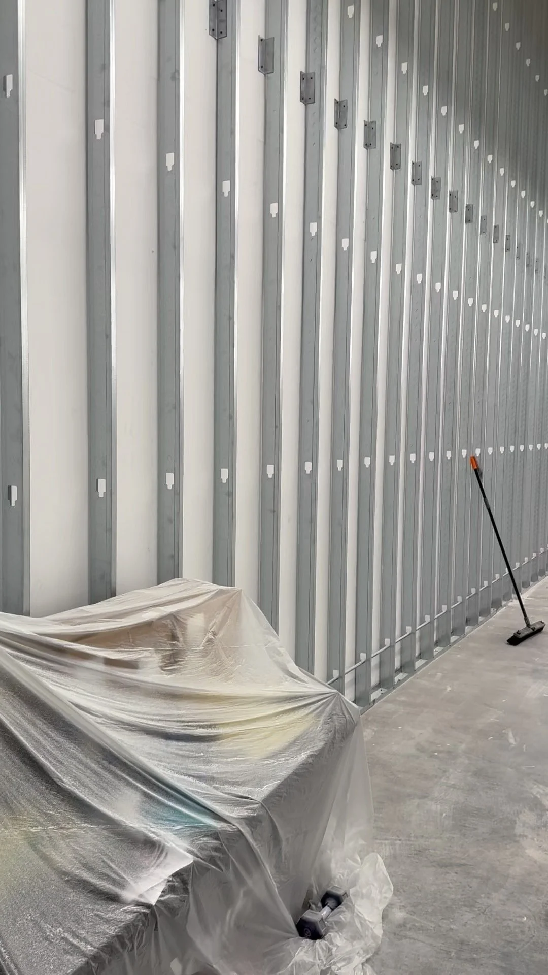 Construction site with metal wall framing, a covered object, and a broom leaning against the wall.