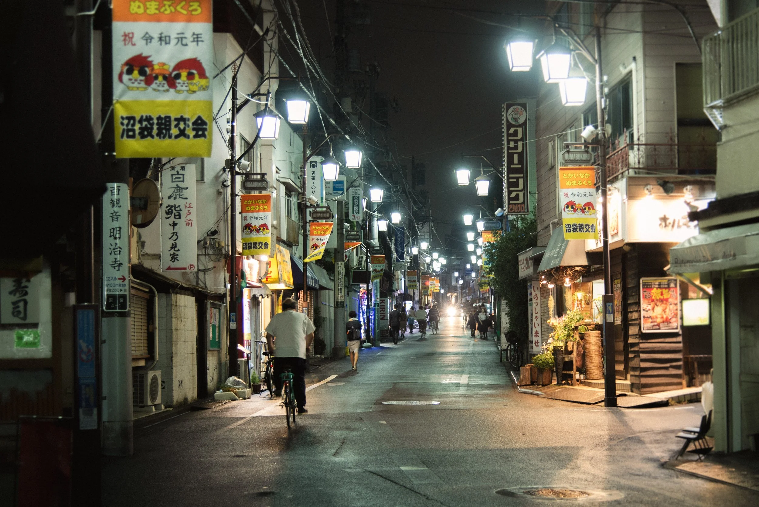 Quiet residential street in Tokyo at night with a cyclist riding under street lamps
