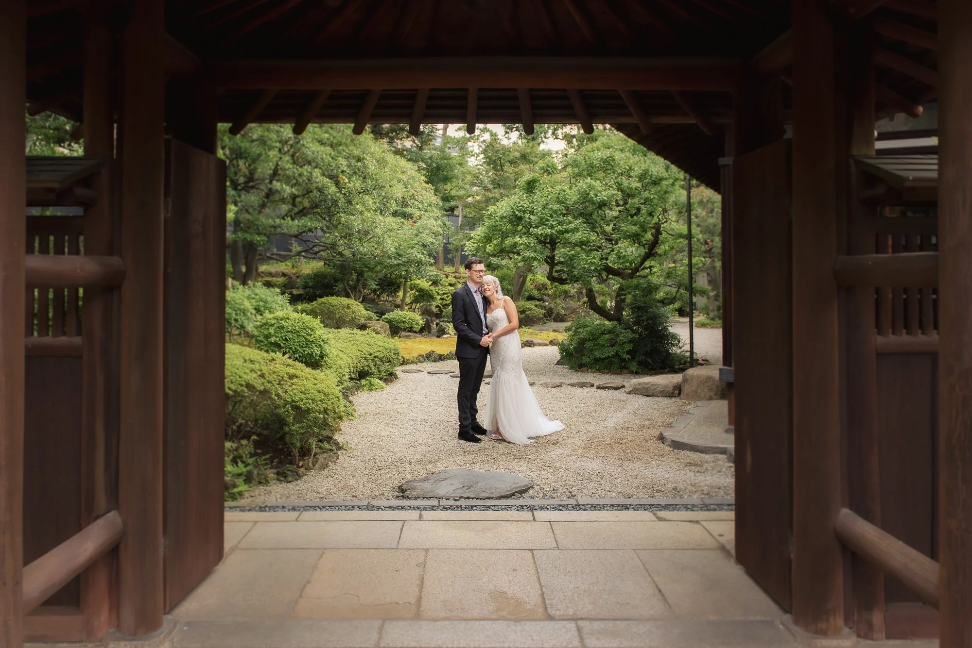 Young couple enjoy an intimate moment in a beautiful Japanese garden, framed by a wooden gate.