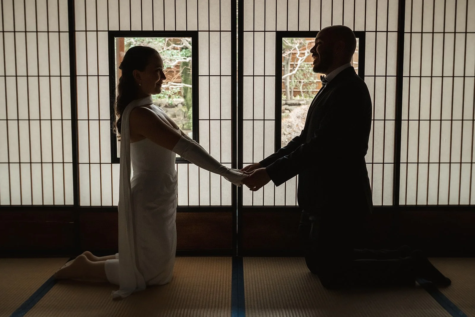 Couple hold hands silhouetted against a bright background.  They are smiling and happy.