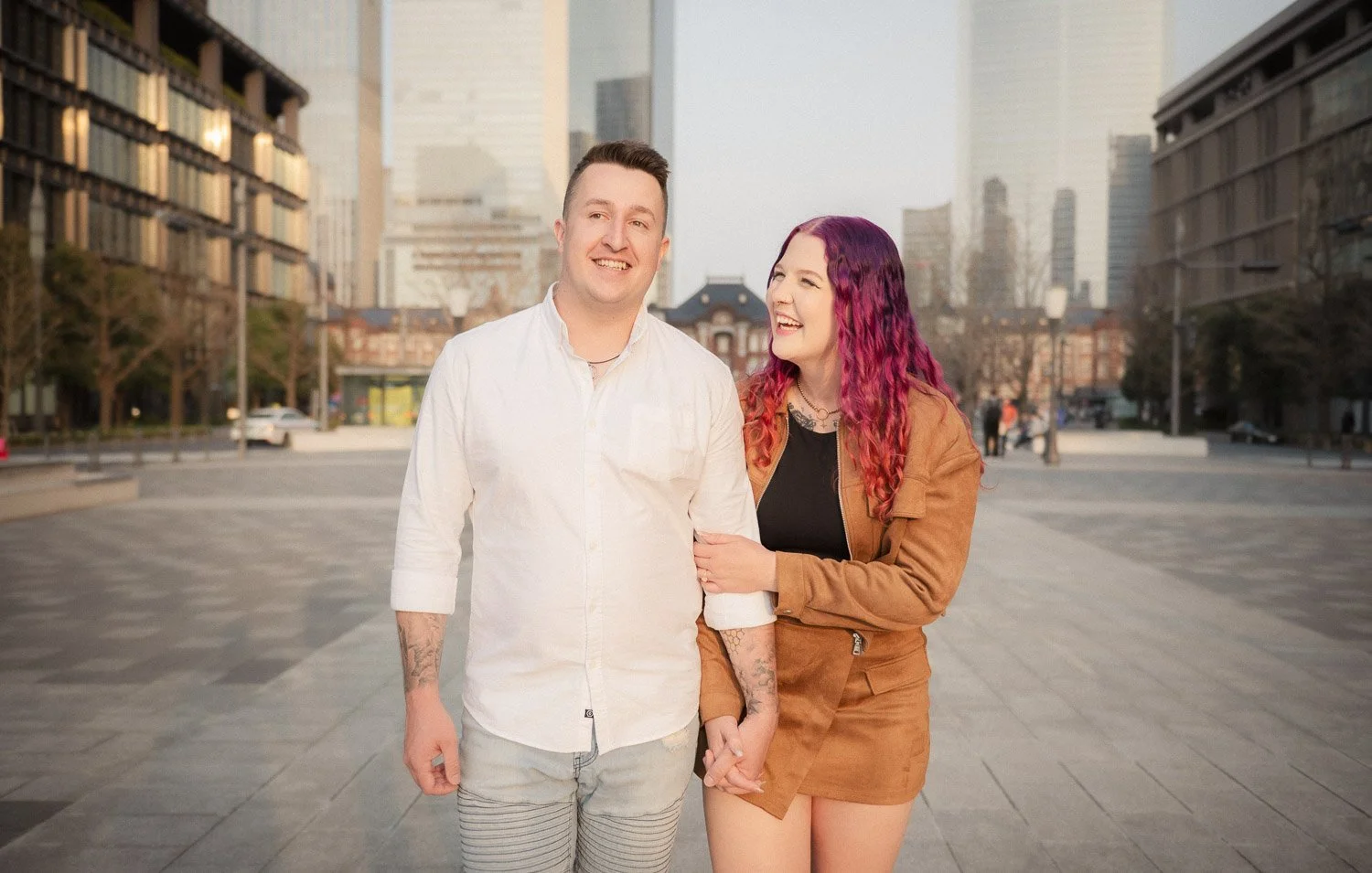 Happy couple walk hand-in-hand along a wide boulevard away from Tokyo station.