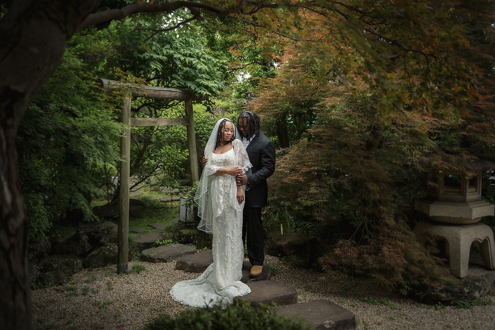 Wedding couple standing together in a quiet Tokyo garden after their elopement ceremony, surrounded by deep green foliage and traditional stone details