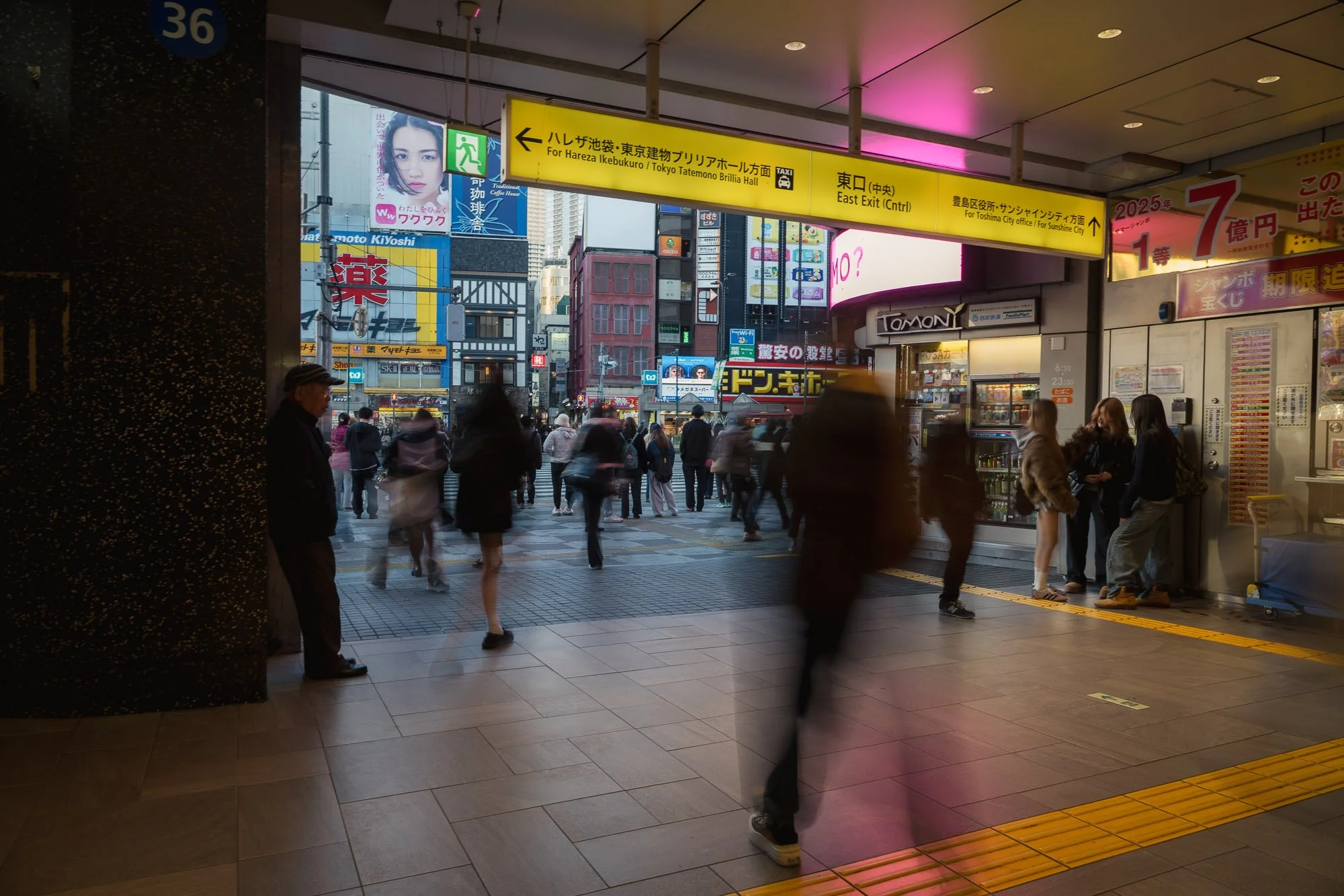 A lone man stands at the entrance of Ikebukuro Station while blurred pedestrians move through the busy Tokyo scene, reflecting culture shock and isolation in Japan.