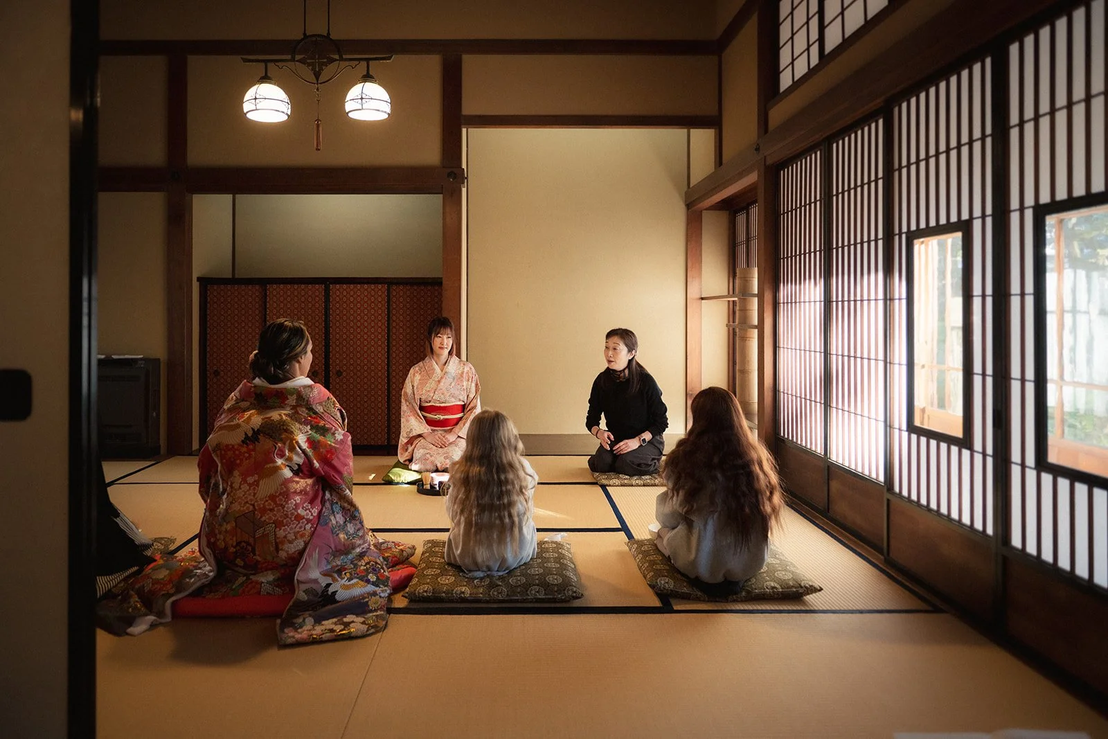 A family enjoy a tea ceremony in a traditional Japanese house.  Light filters through paper screens.  The mood is calm and peaceful.