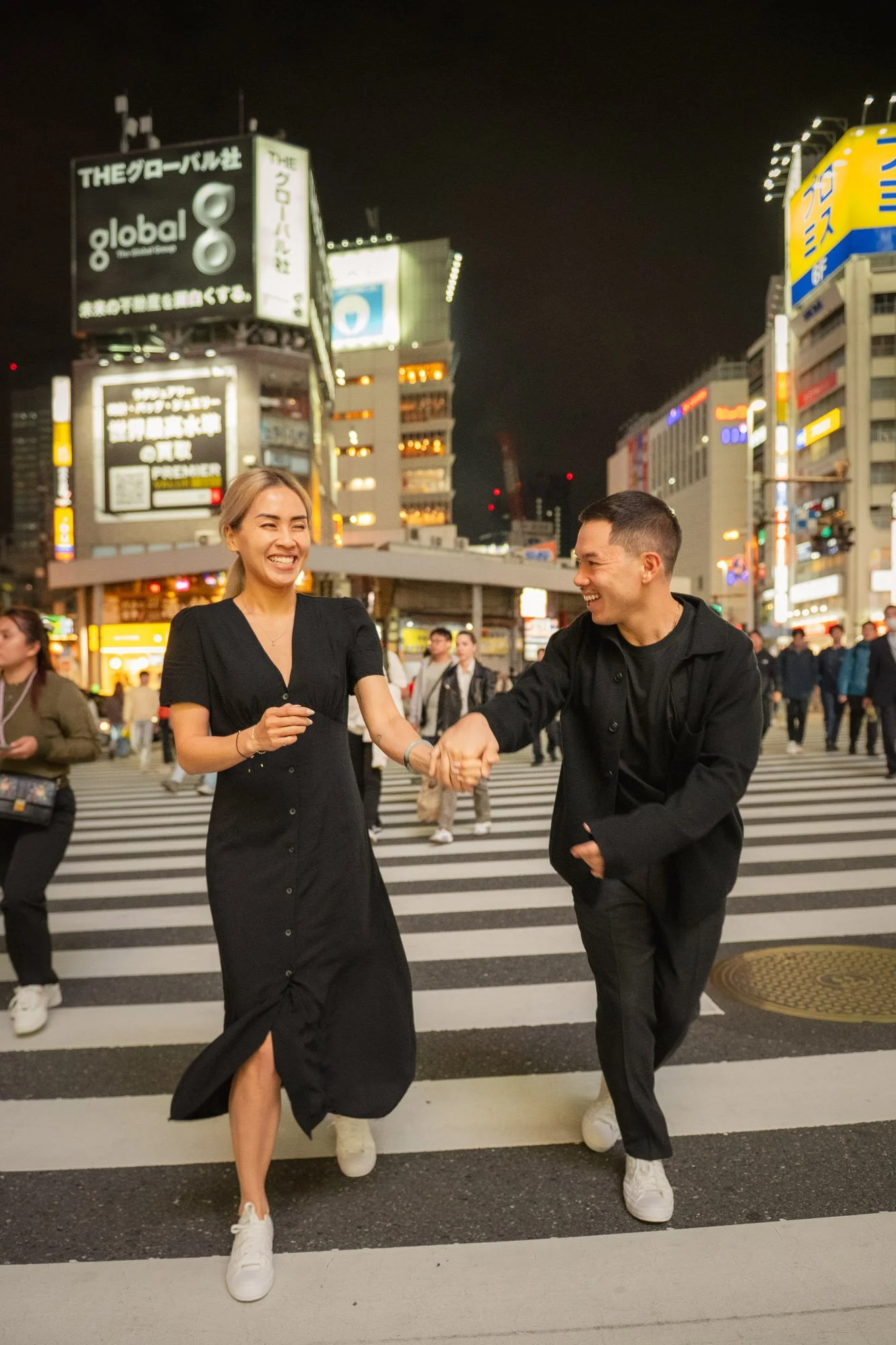A young couple running across a Tokyo road laughing.