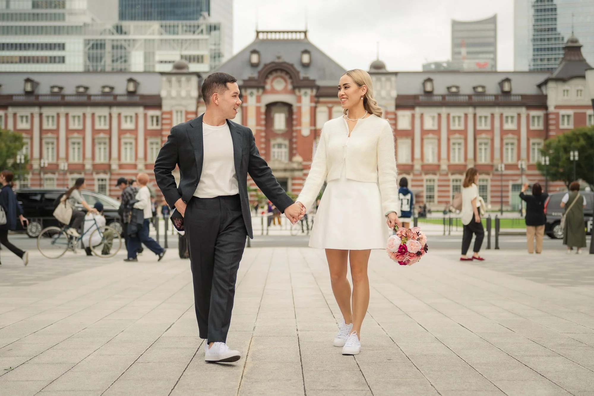 Couple photoshoot at Tokyo Station, holding hands and walking together while looking at each other