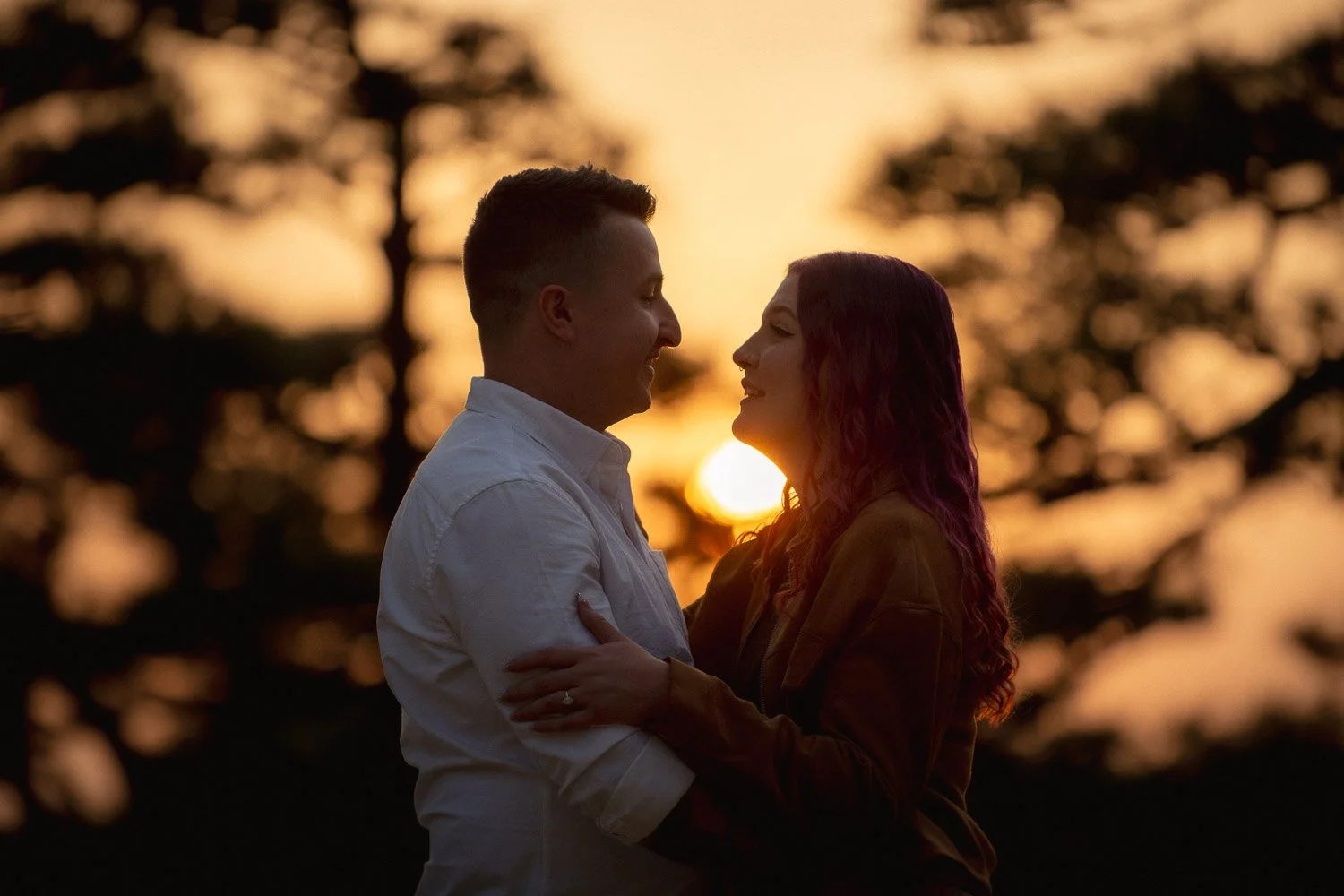 Young couple embrace silhouetted against the setting sun.