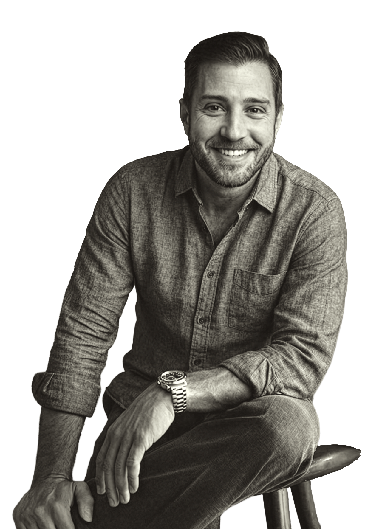 A smiling man with a beard, wearing a long sleeve button-up shirt, sitting on a stool, with his arm resting on his knee. Black and white photo.