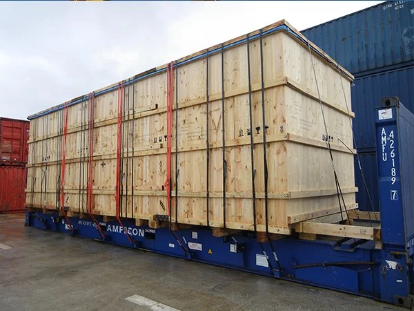 Large wooden crate on a blue transportation flatbed at a shipping yard.