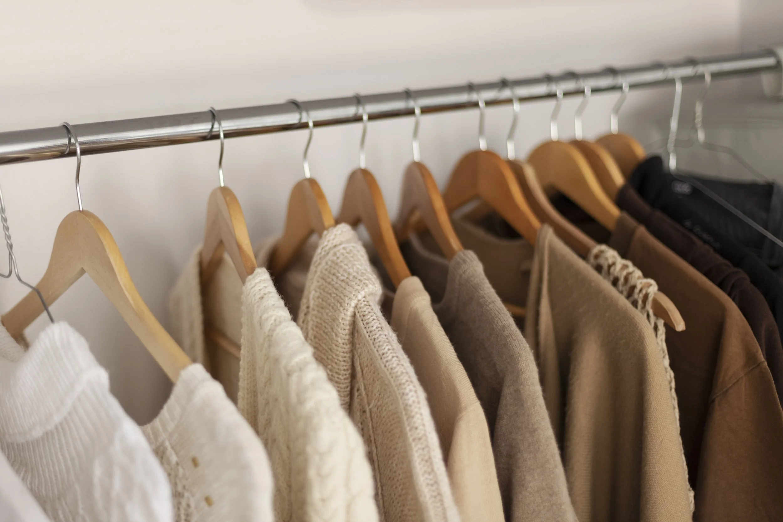 Neutral-toned sweaters and tops hanging on wooden hangers in an organized closet