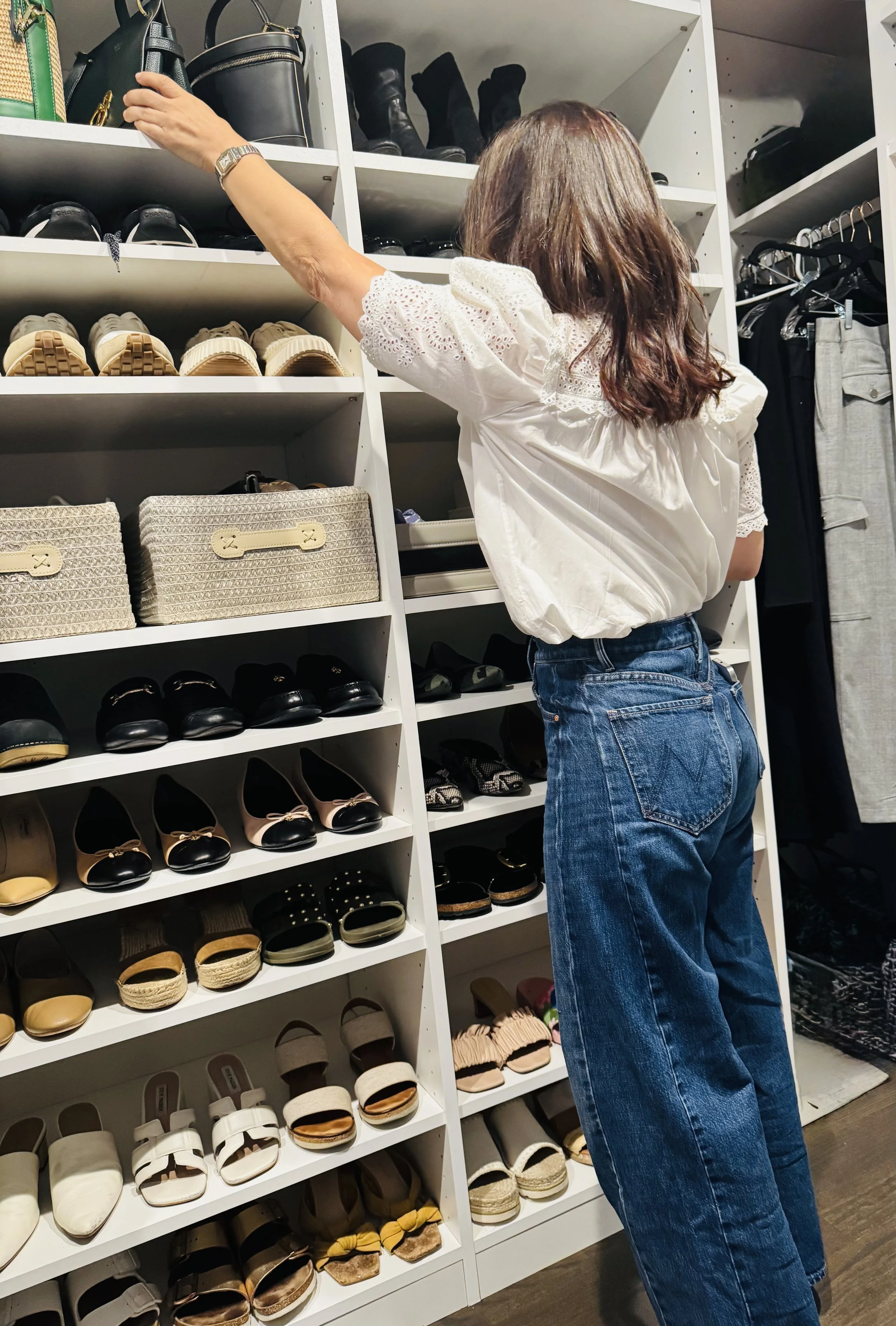 Professional organizer arranging handbags on a custom closet shelf with a neatly styled wall of shoes.