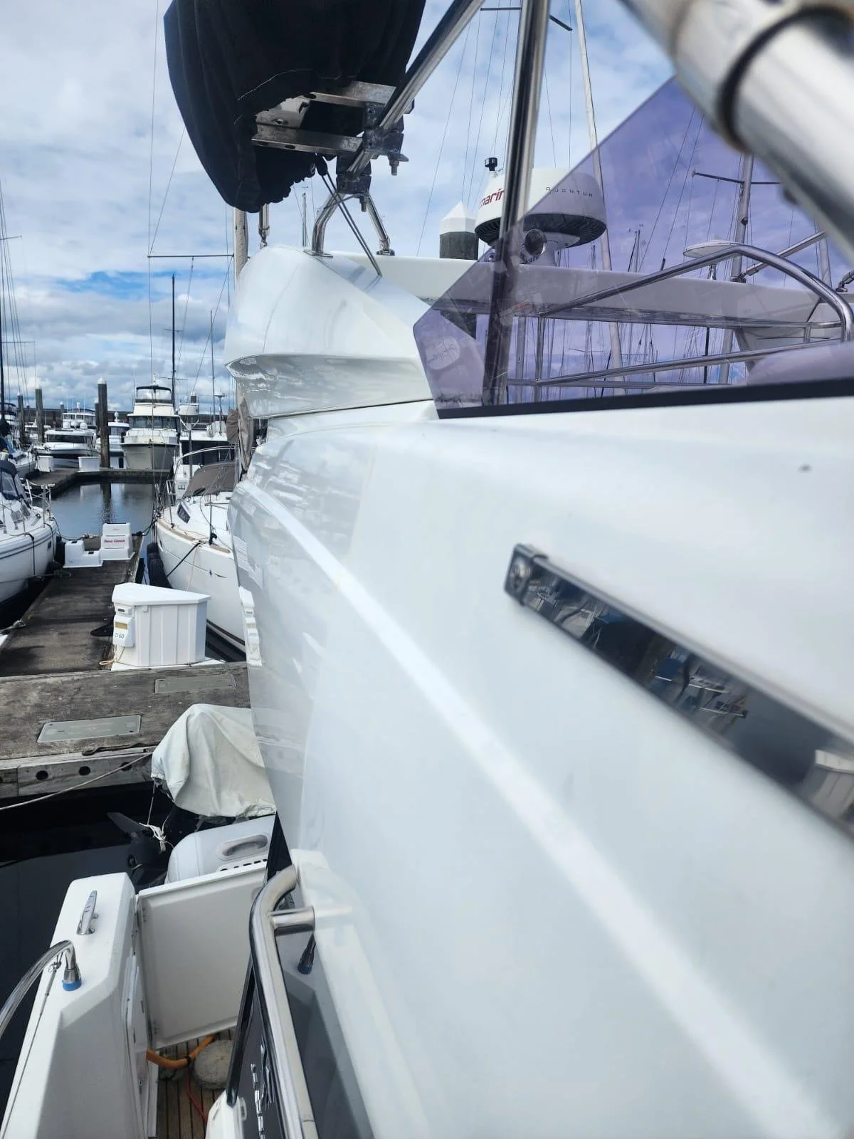 Close-up view of a sailboat at a marina with other boats docked nearby under a partly cloudy sky.