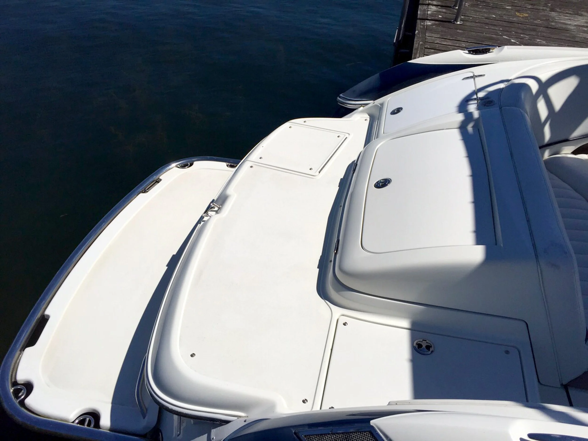 Close-up of the bow of a white yacht docked at a pier, showing storage compartments and a shadow cast on the deck.