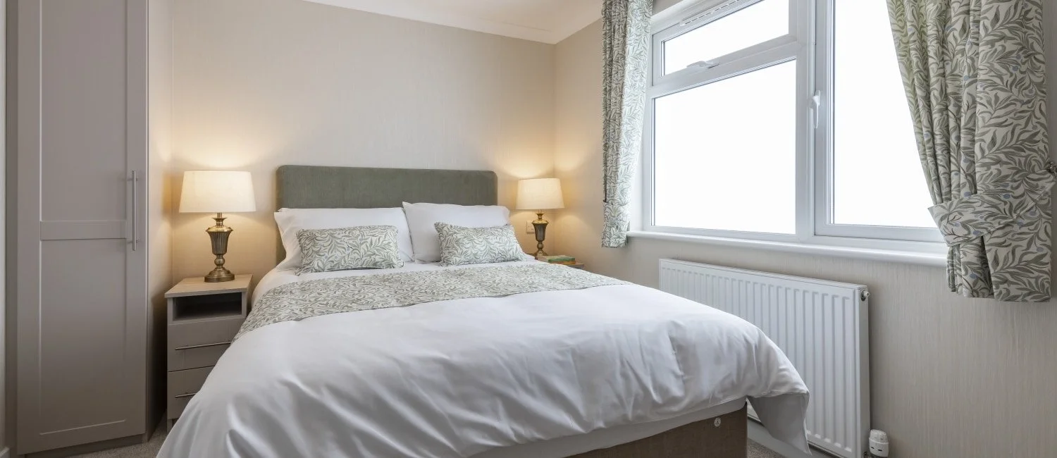 A neatly made bed with white bedding and decorative pillows in a bedroom with a window and patterned curtains.