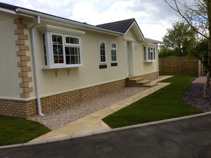 Front view of a newly renovated house with a cream-colored exterior, brick foundation, and a well-maintained lawn with a paved pathway leading to the front door.