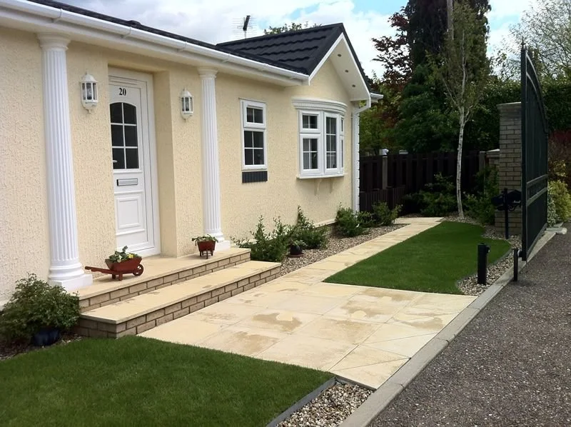 Front entrance of a house with white columns, a white door, and a pathway leading to a gate.