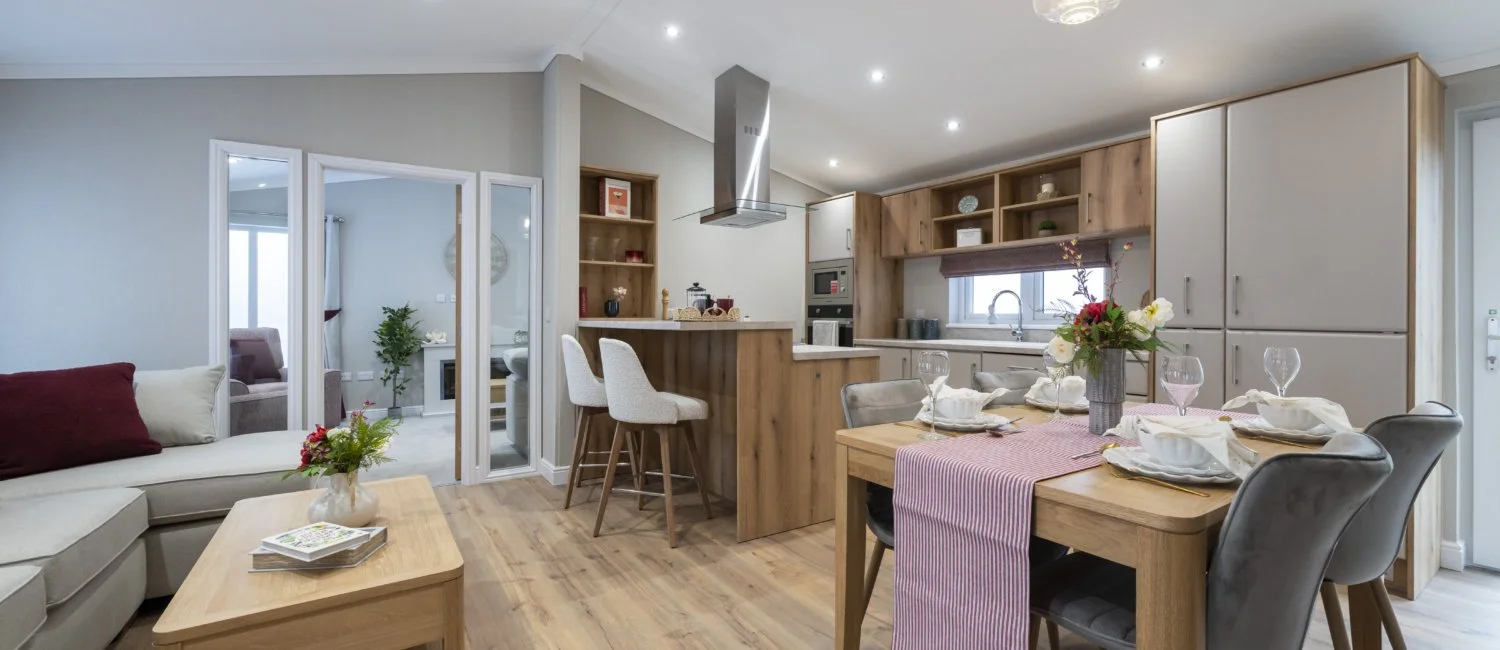 Open concept kitchen and dining area with wooden accents, a table set with white dishes and napkins, a floral centerpiece, and a white sofa with cushions in the living area.