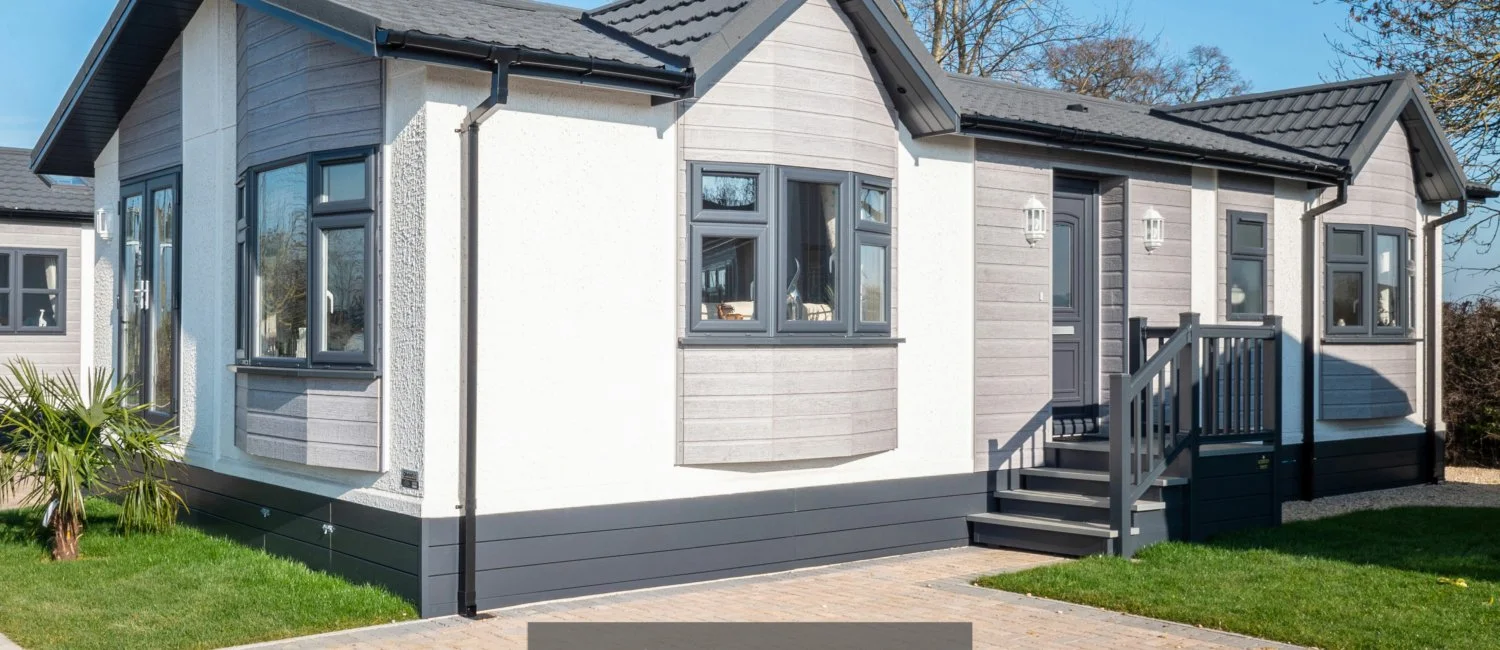 A modern house with gray siding and white stucco walls, gray trim, a small front porch, stairs, and a lawn, under a clear sky.