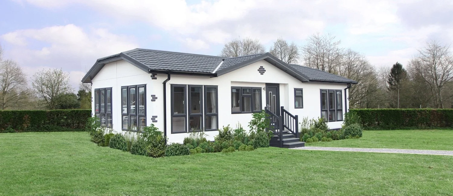 A modern white house with black trim and stairs, surrounded by a green lawn and bushes, under a partly cloudy sky.