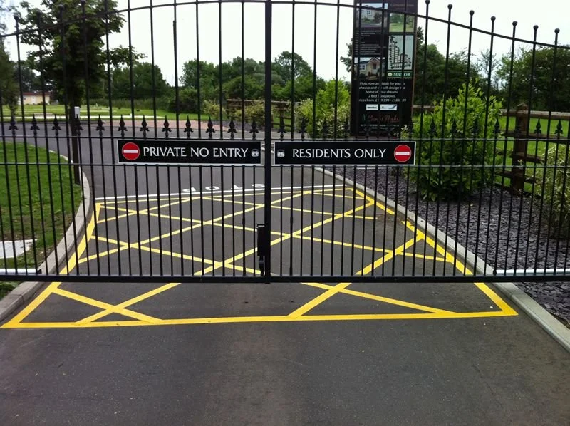 Gated entrance with signs indicating private no entry and residents only, featuring a black iron gate and yellow parking restrictions painted on the asphalt road.