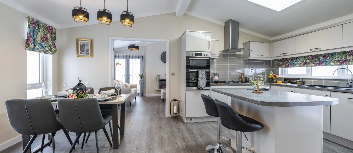 Modern kitchen and dining room with gray chairs, white cabinets, gray tiled backsplash, kitchen island with seating, and decorative window treatments.