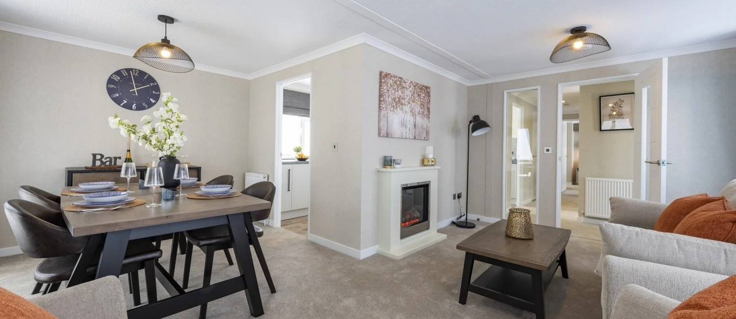 Living room with beige walls, a fireplace, a dining table with six chairs, and a sitting area with beige and orange couches, a coffee table, and wall art.