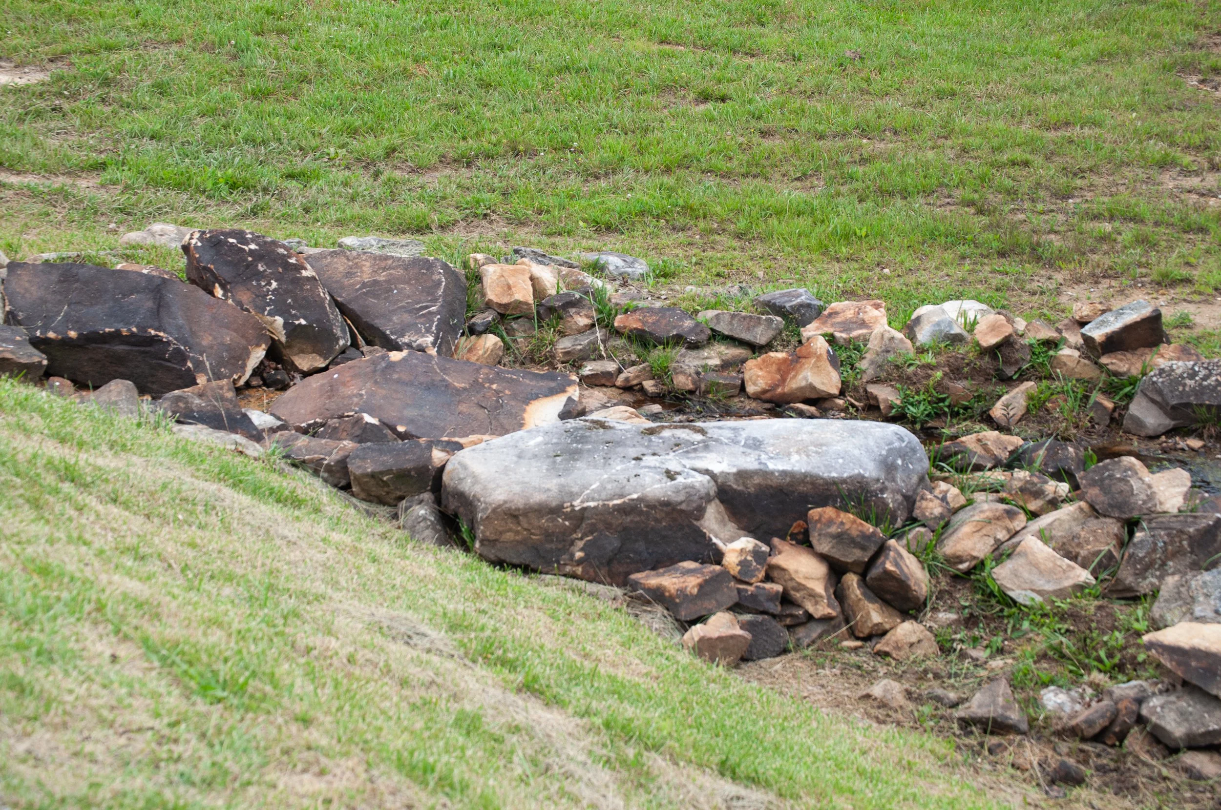A small stream bordered by rocks with grass and soil surrounding it.