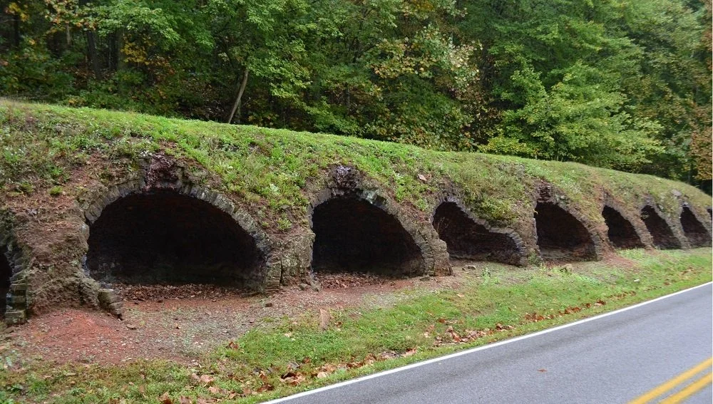 Old stone tunnel arches built into a grassy hillside beside a road, surrounded by trees.