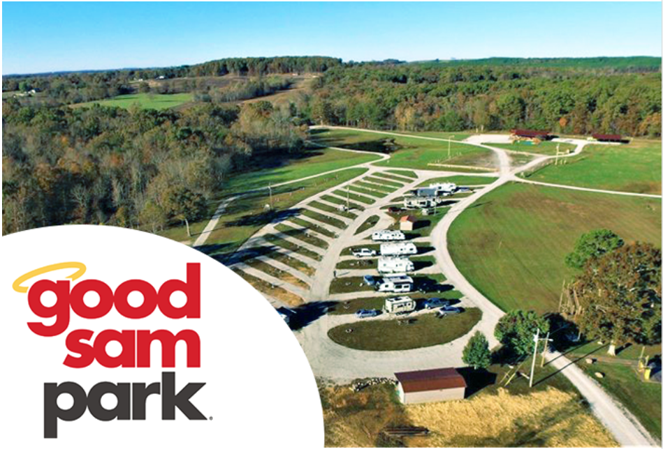 Aerial view of a campground with RVs, trailers, and tents on grassy areas, surrounded by trees and rolling hills, with the "good sam park" logo in the lower left corner.