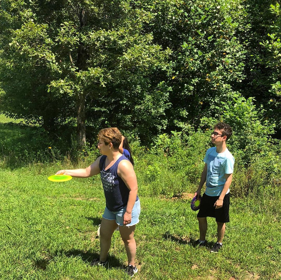 Two children playing with frisbees in a grassy outdoor area with trees.