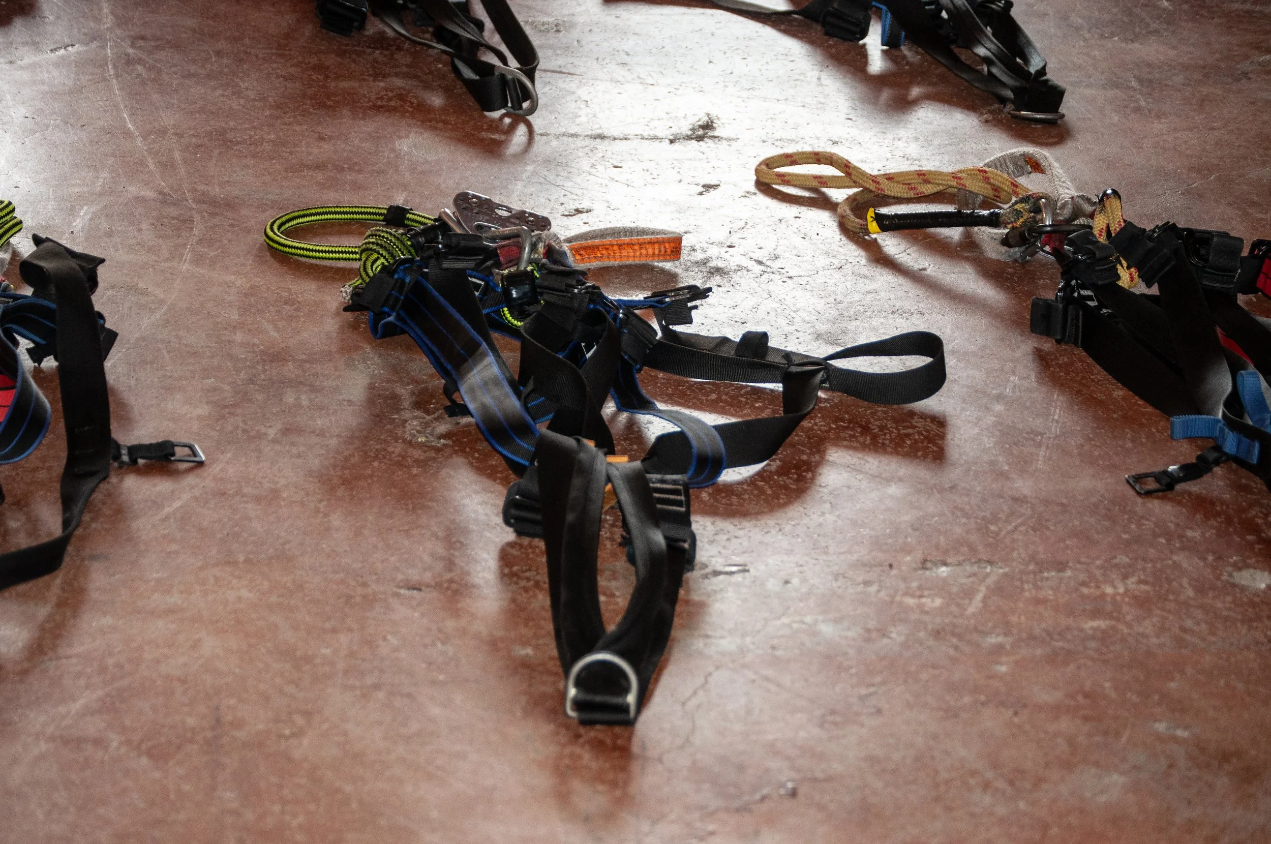 Climbing harnesses and gear laid out on a concrete floor.