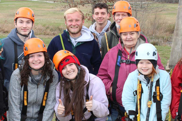 Group of smiling people wearing safety helmets and harnesses outdoors, likely on a climbing or ziplining adventure.