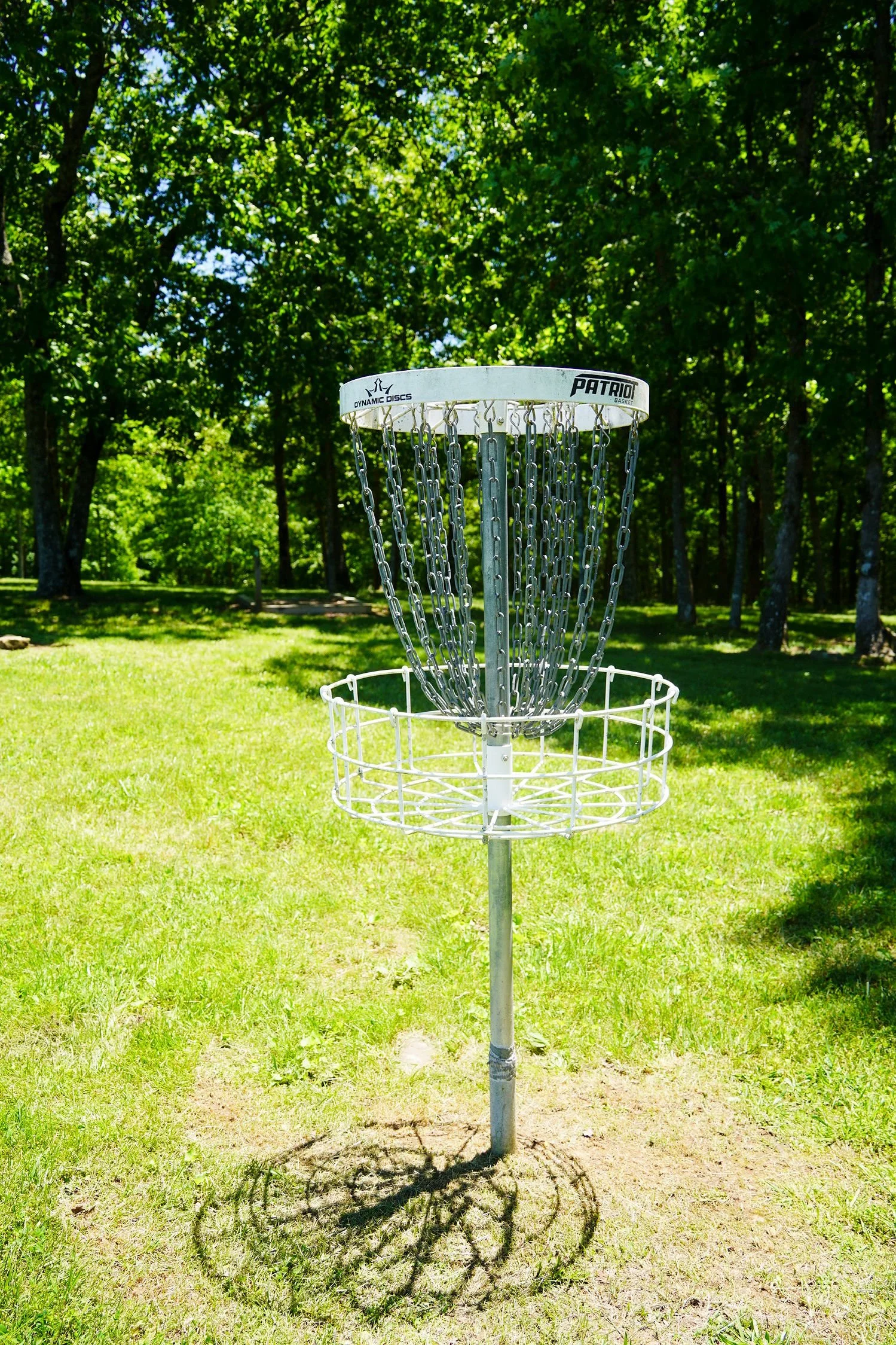 Disc golf basket on grassy field with trees in the background.