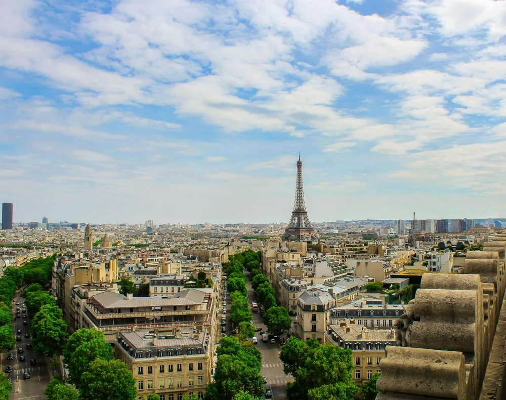 Paris, utsikt över staden med Eiffeltornet i centrum, omgiven av byggnader och träd, mot en himmel med spridda moln.