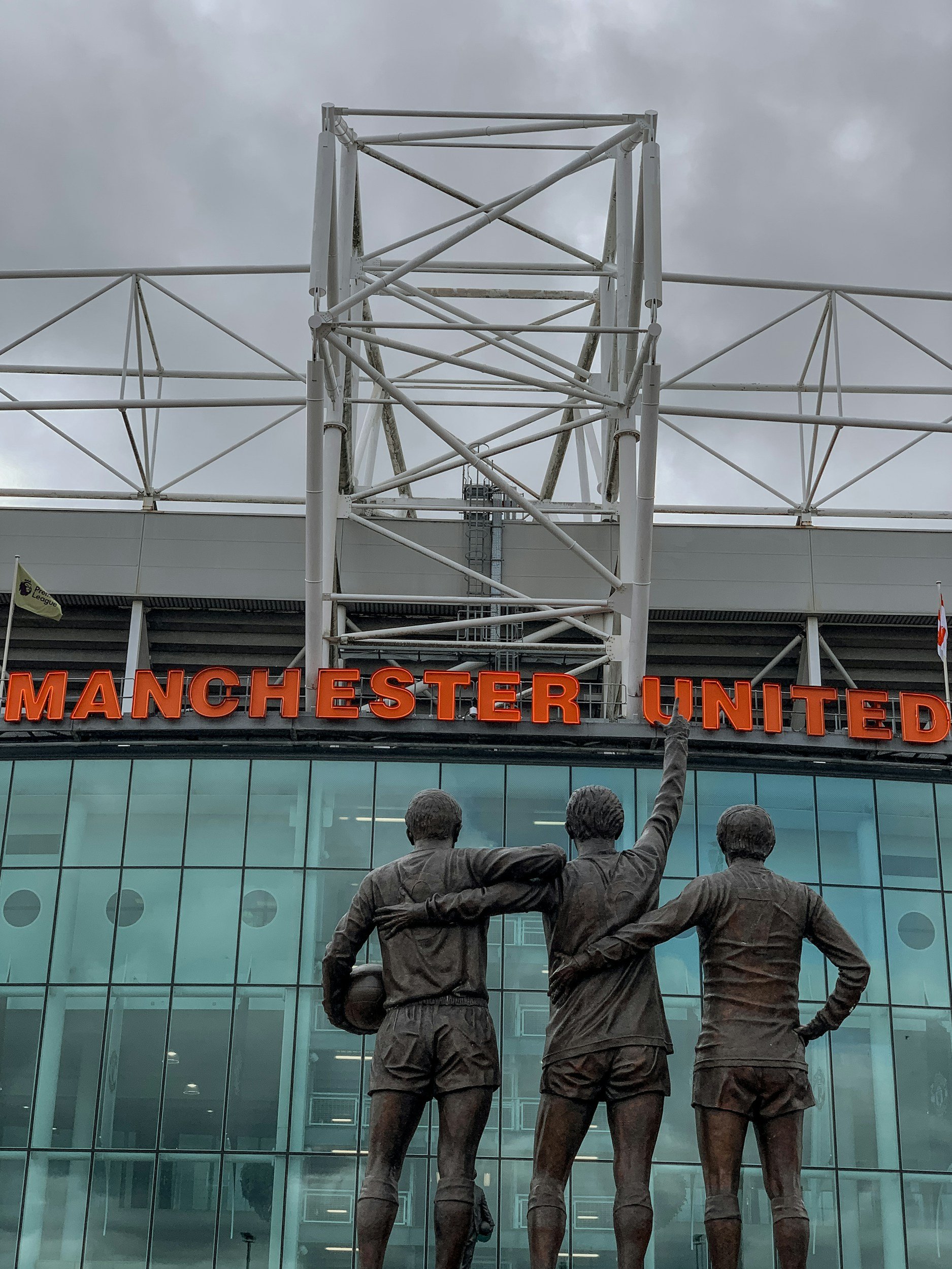 Staty av tre fotbollsspelare framför Manchester Uniteds stadion