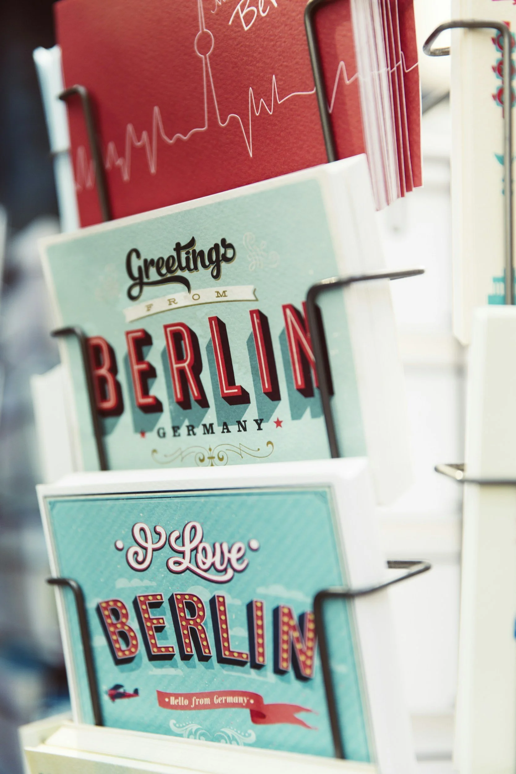 Kort med texten "Greetings from Berlin, Germany" och andra utformade postcards i en butikshylla.