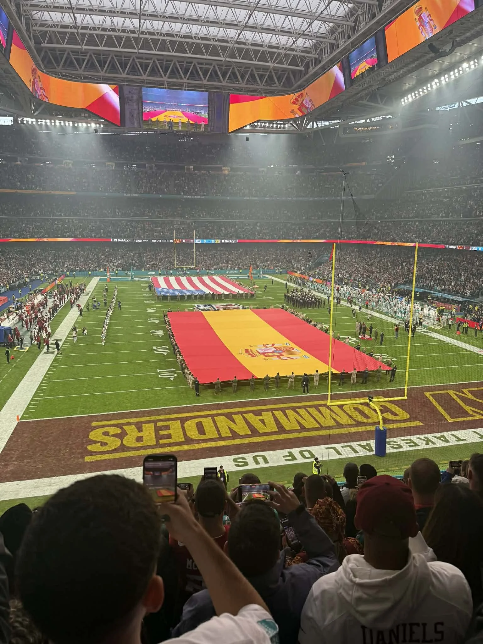 Publik i en stadion förbereder sig för en amerikansk fotbollsmatch med en stor spansk flagga på planen