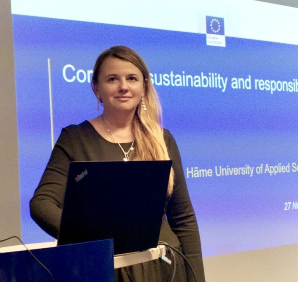 A woman standing in front of a presentation screen with the European Union flag, giving a presentation at Hame University of Applied Sciences on sustainability and responsibility.